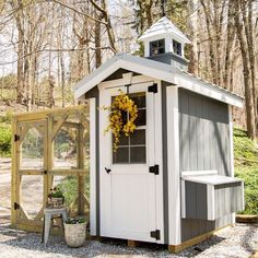 a small shed with a clock on the side and a potted plant in front