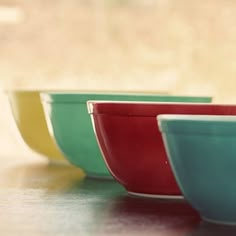 four colorful bowls are lined up on a table top, with one empty bowl in the middle