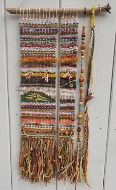 two weavings hanging on a white wall next to a wooden stick and some beads