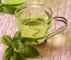 a glass cup filled with green tea sitting on top of a woven table cloth next to some leaves