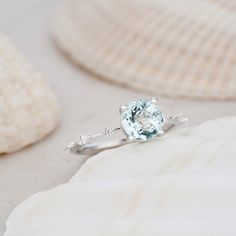 a white gold ring with an aqua blue topazte surrounded by pearls and seashells