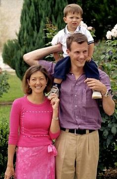 a man, woman and child posing for a photo in front of some bushes with flowers