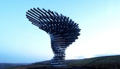 a large metal sculpture sitting on top of a dirt field next to a green hillside