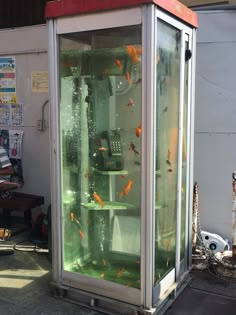 a phone booth with goldfish in it and people sitting on the bench behind it