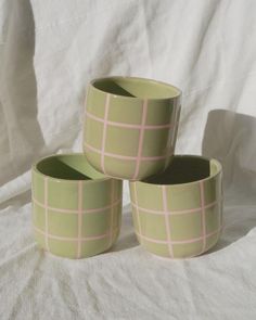 three green bowls with pink lines on them sitting on a white sheeted surface,