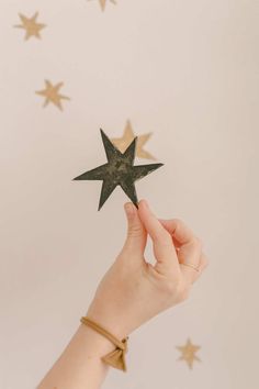 a hand holding a star shaped object in front of some gold stars on the wall