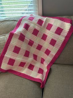 a pink and white blanket sitting on top of a couch next to a windowsill