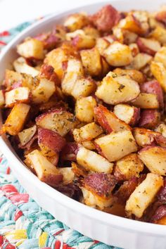 a white bowl filled with cooked potatoes on top of a colorful table cloth next to a fork