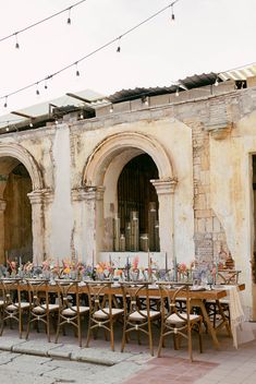 an outdoor dining area with tables and chairs set up in front of the building, surrounded by string lights