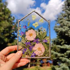 a hand holding up a small glass house with flowers in it