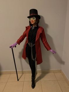 a woman in a red coat and top hat holding a cane with her hands out