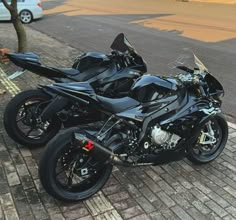 two motorcycles are parked on the side of the road next to each other in front of a tree