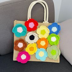 a handbag with crocheted flowers on it sitting on a couch next to a pillow