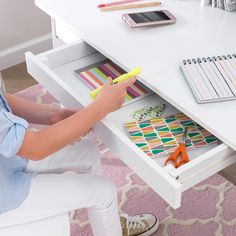 a person sitting at a desk with some colored pencils and markers in their drawer