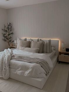 a white bed with pillows and blankets on top of it in a bedroom next to a window