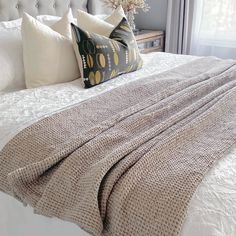 a bed with white linens and pillows on top of it next to a window