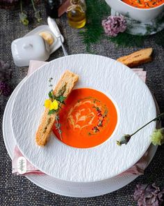 there is a bowl of soup with bread on the plate and flowers in the background