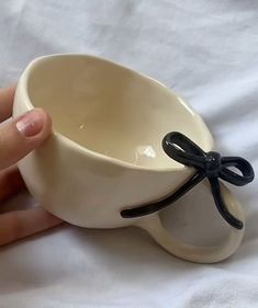 a hand holding a white bowl with a black bow on it