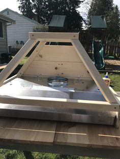 a wooden table topped with a metal pan on top of it's side in the yard