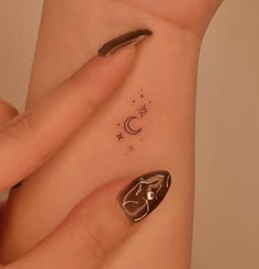 a woman's hand with a small tattoo on her left wrist and the moon in the sky