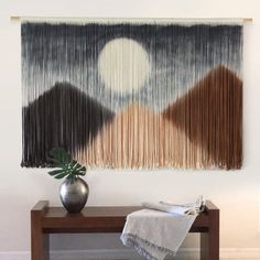 a table with a vase on top of it next to a wall hanging that has an abstract design