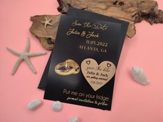 two wedding rings on top of a black save the date card next to starfish