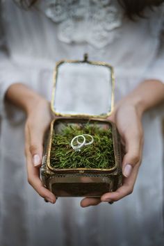 a person holding a box with moss and two wedding rings in it