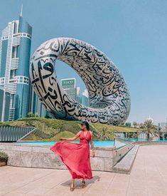 a woman in a red dress is standing near a large sculpture