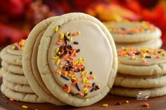 cookies with sprinkles and white frosting on a wooden board next to fall leaves