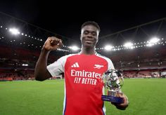 a man holding a trophy in his right hand and wearing a red shirt with white lettering on it