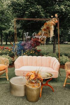 a pink couch sitting on top of a grass covered field next to chairs and tables