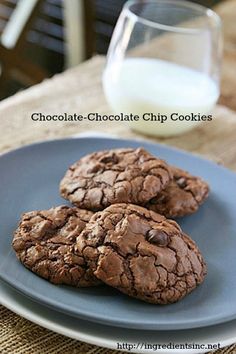 three chocolate cookies on a blue plate with a glass of milk next to it,