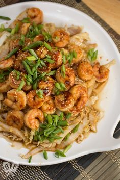 a white plate topped with shrimp and noodles on top of a bamboo mat tablecloth