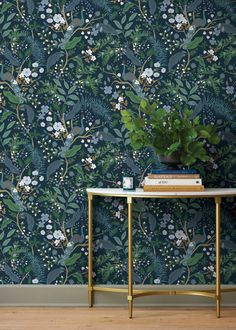 a table with books and a plant on it in front of a floral wallpaper