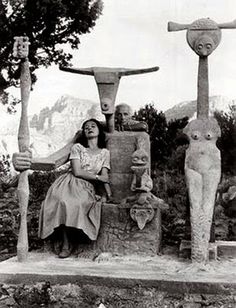 an old black and white photo of a woman sitting in front of some strange statues