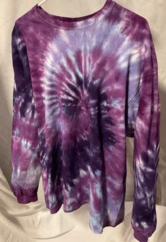 a purple and blue tie - dyed shirt hanging on a white background with the top half rolled up