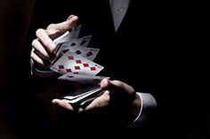 a man in a tuxedo holding playing cards and cell phone with both hands