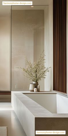 a white bath tub sitting under a window next to a vase with flowers in it