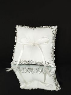 a white ring pillow with a bow on the front and ribbon at the back, sitting on a reflective surface