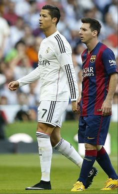 two soccer players walking on the field during a game with an audience in the background