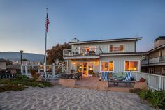 a beach house is lit up by the sun at dusk, with chairs and tables in front of it