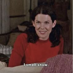 a woman sitting on top of a bed in a red shirt with the caption i smell snow