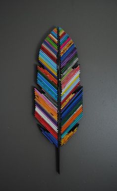 a multicolored leaf shaped brooch hanging on a gray wall next to a pair of scissors