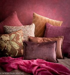 a pile of pillows sitting on top of a bed next to a pink blanket and wall