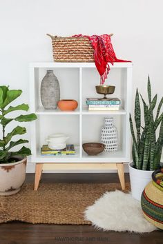 a white bookcase with plants and baskets on top