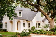 a white house surrounded by trees and plants in front of the house is an oak tree