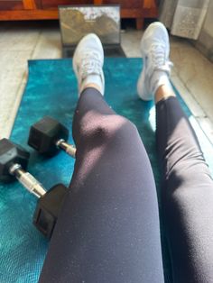 the legs of a person who is sitting on a mat with dumbbells in front of them