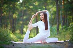 a woman is doing yoga outside in the woods with her arms up and legs crossed