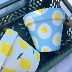 two cups with lemons painted on them are sitting in a green basket next to each other