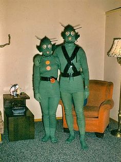 two people dressed as aliens standing next to each other in front of a couch and chair